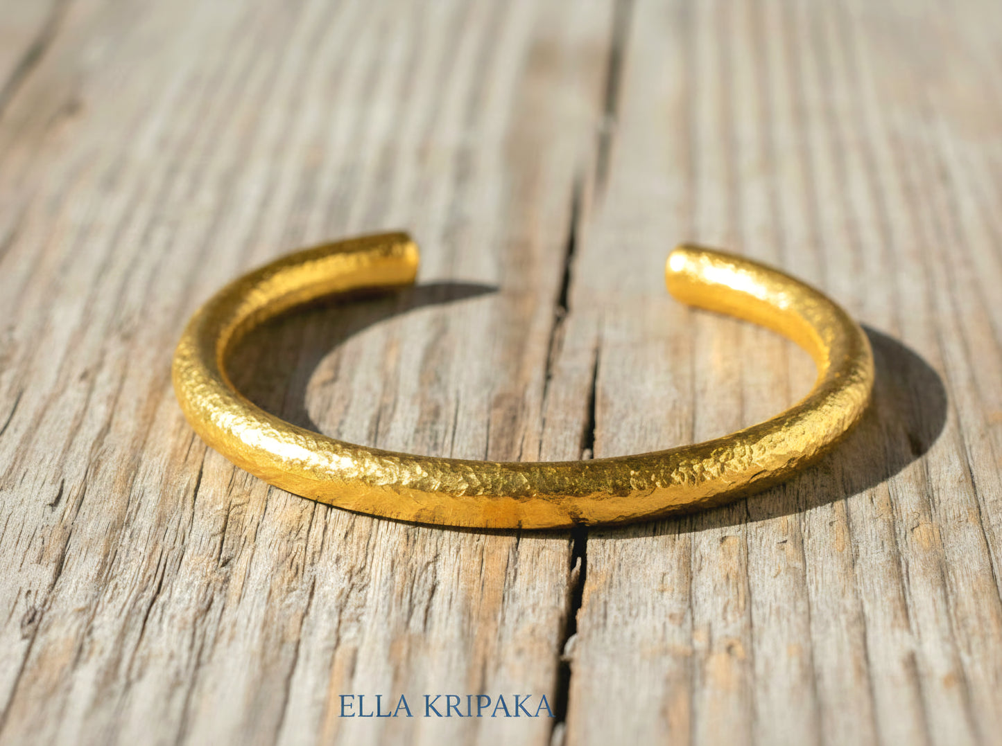 24k 9999 gold hammered Ancient Rome thick cuff bracelet on a grey old wooden surface, branded 'Ella Kripaka'