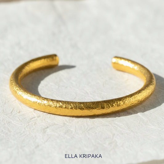 24k gold hammered rounded thick cuff bracelet on a white rise paper surface, branding artist 'Ella Kripaka'
