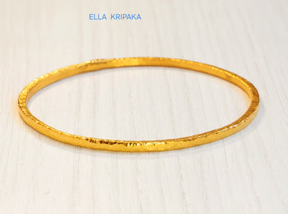 22k gold hammered two thick bangles bracelets Ancient Rome style on a white wooden surface, artist-jeweler 'Ella Kripaka' branding
