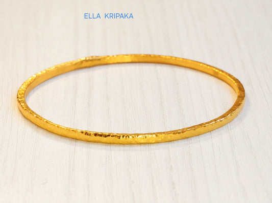 22k gold hammered two thick bangles bracelets Ancient Rome style on a white wooden surface, artist-jeweler 'Ella Kripaka' branding