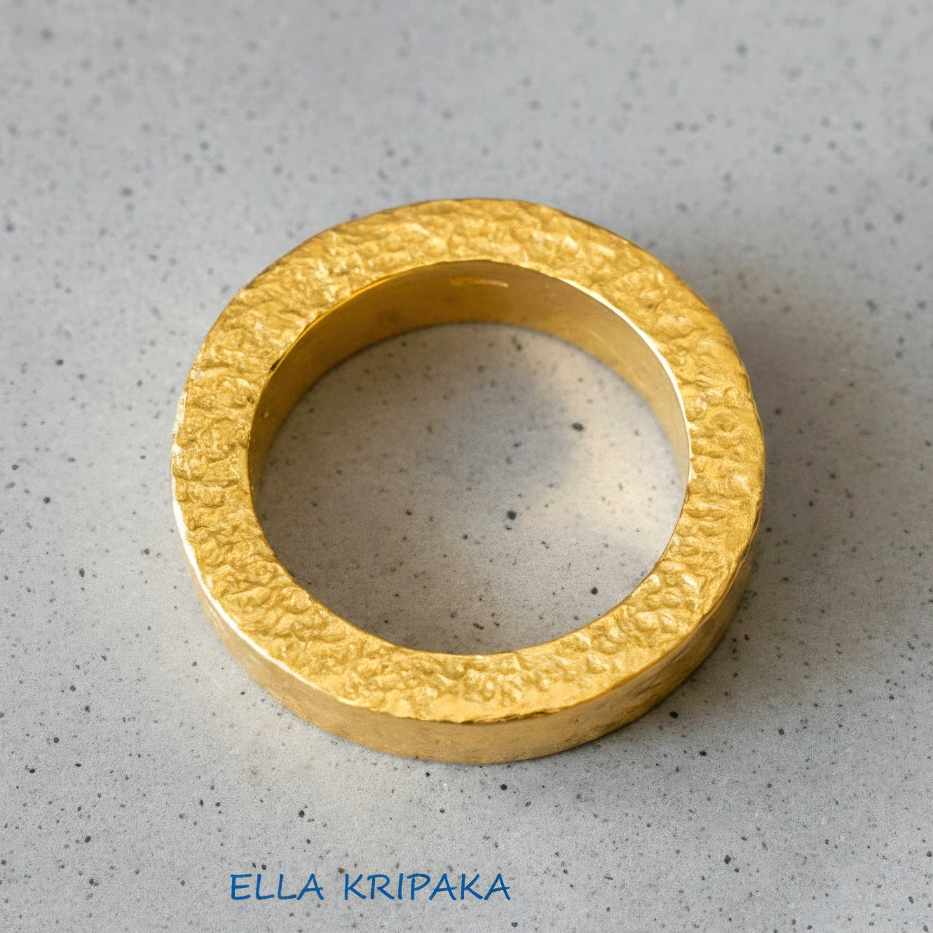 Hammered 24k Gold 9999 gold Ancient Rome  thick ring with textured gold on a grey concrete background, branded 'Ella Kripaka'