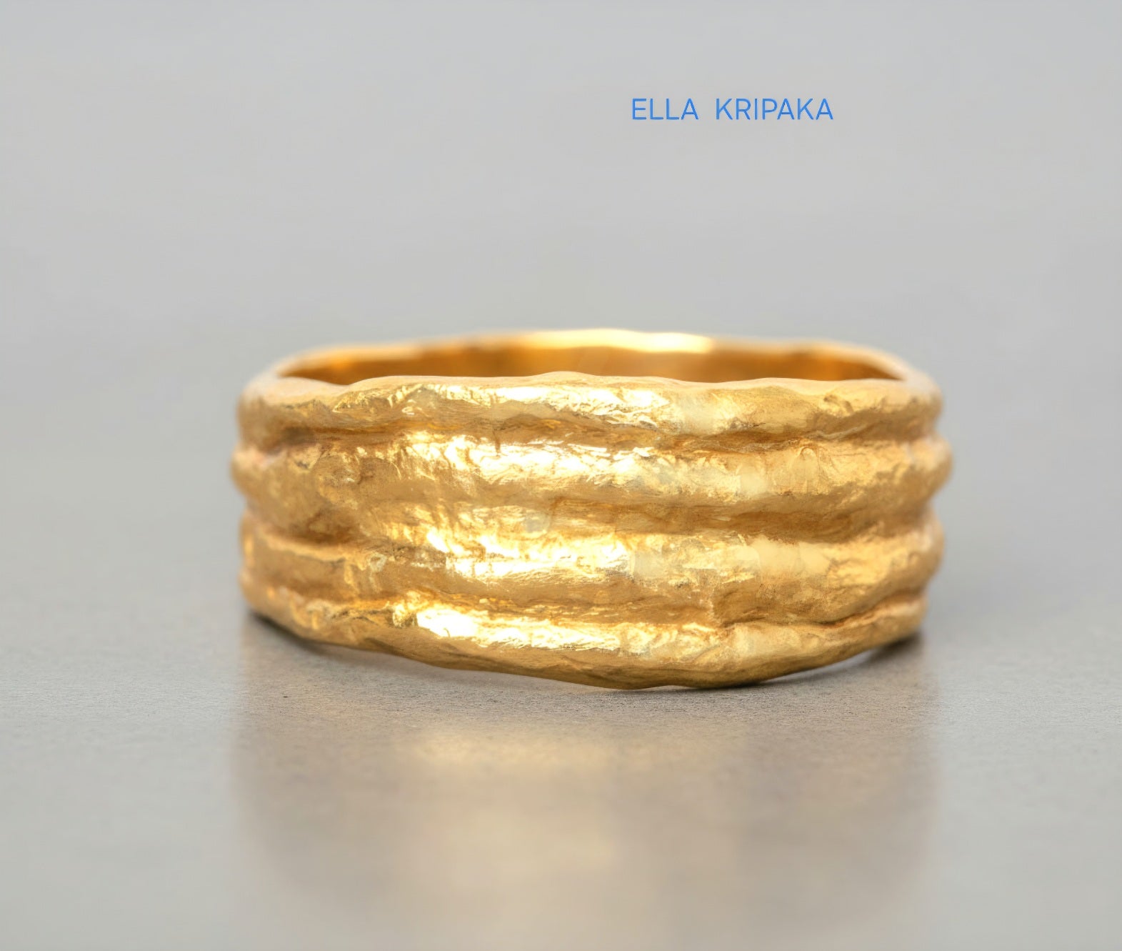 Organic hammered 24k 9999 gold convex ring with uneven thick edges on grey surface, artist-jeweler's name 'Ella Kripaka' is written in picture