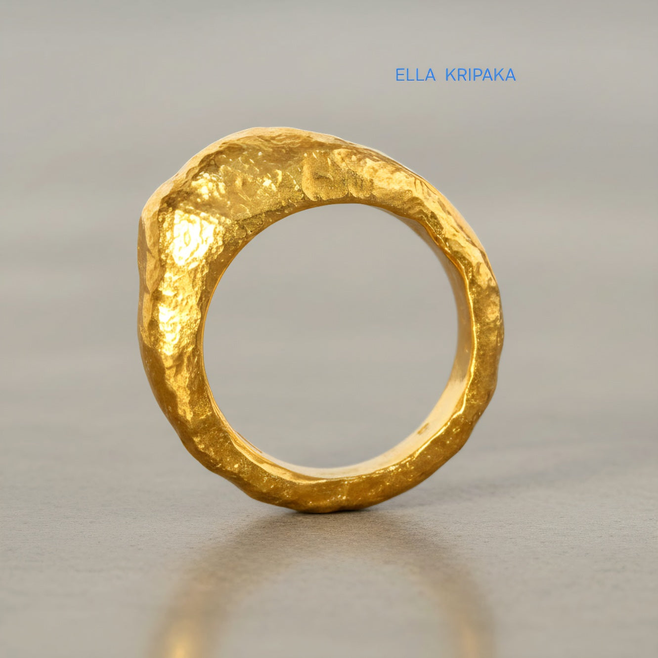 Hammered organic 24k Gold 9999 gold uneven signet thick ring with textured gold on a grey concrete background, branded 'Ella Kripaka'