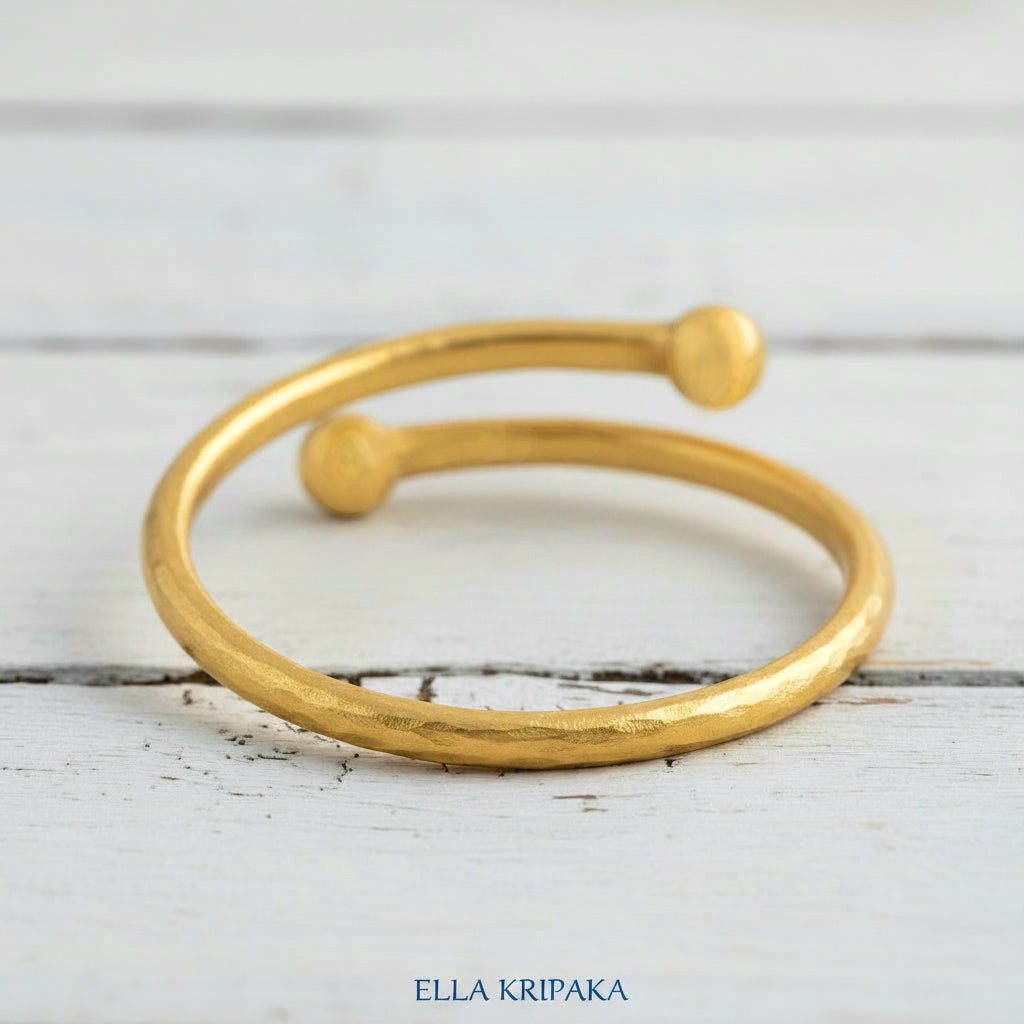 Twisted 24k gold hammered bracelet with thick convex rounds ends on white rustic wooden surface, branded artist-jeweler 'Ella Kripaka'