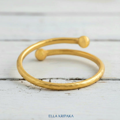 Twisted 24k gold hammered bracelet with thick convex rounds ends on white rustic wooden surface, branded artist-jeweler 'Ella Kripaka'