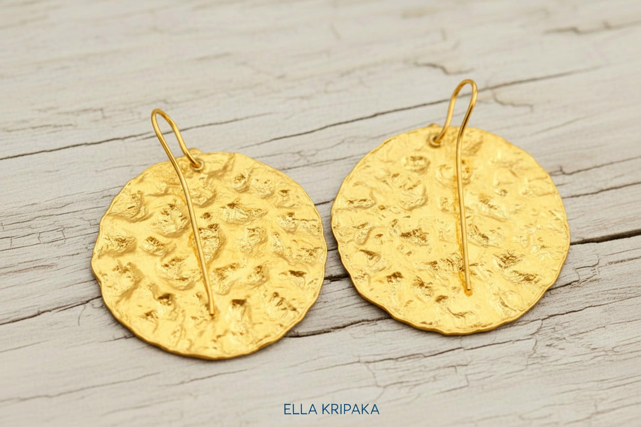 Organic 24k 9999 gold hammered wavy disk earrings with shiny gold textures are on white old wooden background, artist-jeweler's name 'Ella Kripaka'