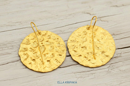 Organic 24k 9999 gold hammered wavy disk earrings with shiny gold textures are on white old wooden background, artist-jeweler's name 'Ella Kripaka'