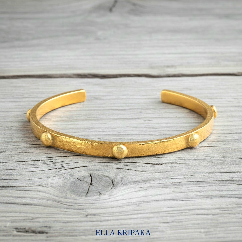 24k gold hammered cuff textured bracelet with convex rounds on light rustic wooden surface, artist 'Ella Kripaka' branding
