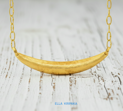 Hammered 24k gold convex Moon pendant with chain on a white rustic wooden background with 'Ella Kripaka' branding