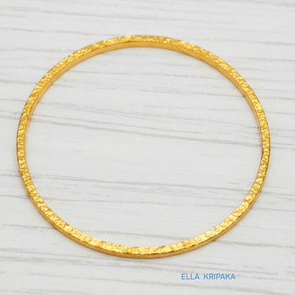 22k gold hammered two thick bangles bracelets Ancient Rome style on a white wooden surface, artist-jeweler 'Ella Kripaka' branding
