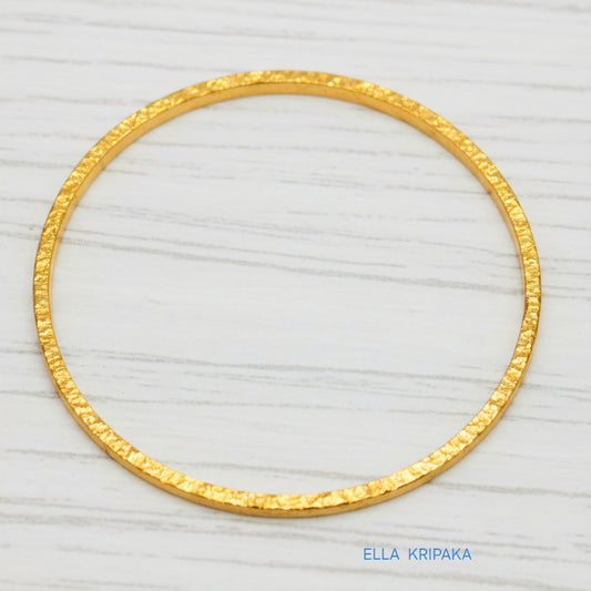 22k gold hammered two thick bangles bracelets Ancient Rome style on a white wooden surface, artist-jeweler 'Ella Kripaka' branding
