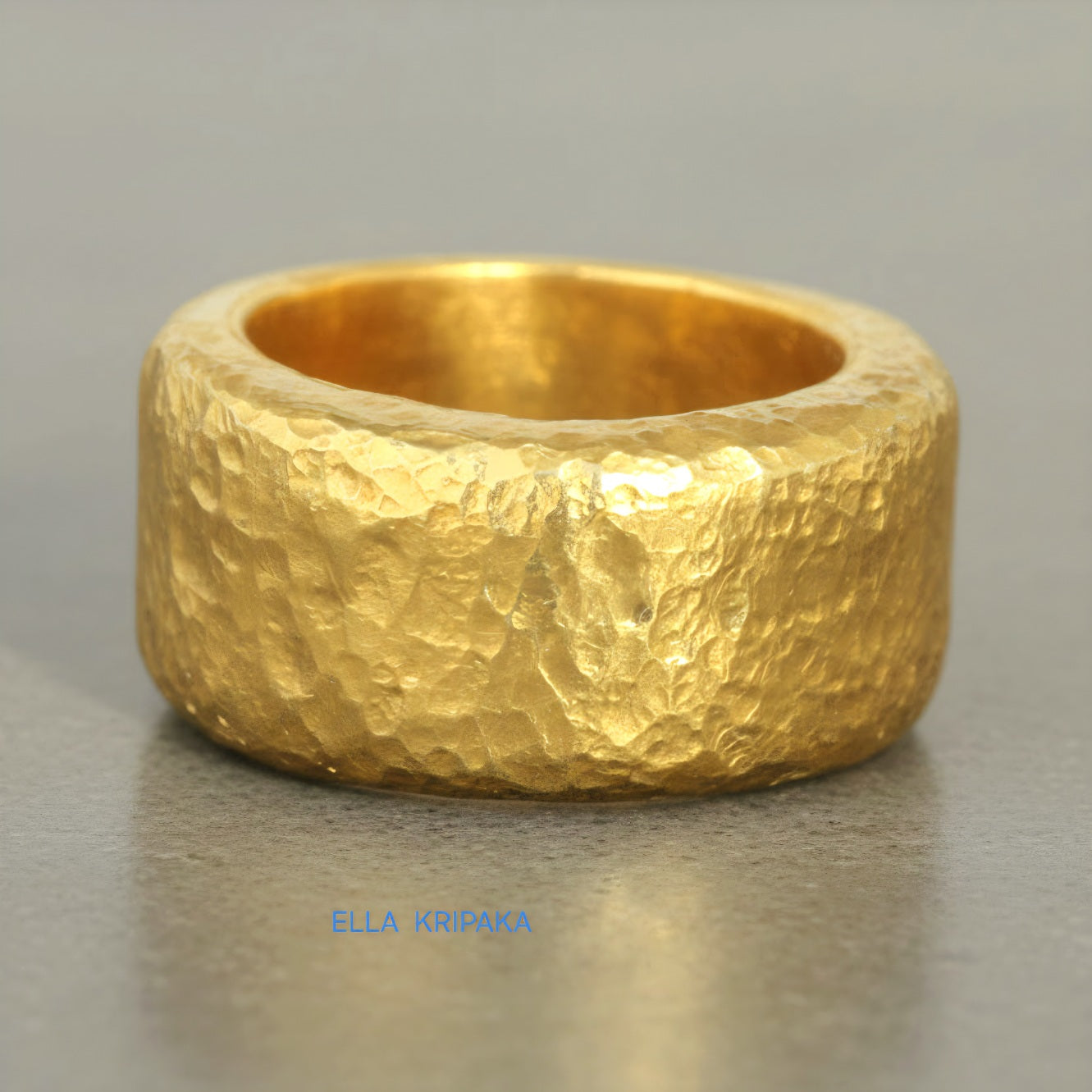 Hammered 24k Gold 9999 gold ring band thick heavy and with textured surface on a grey concrete background, branded 'Ella Kripaka'