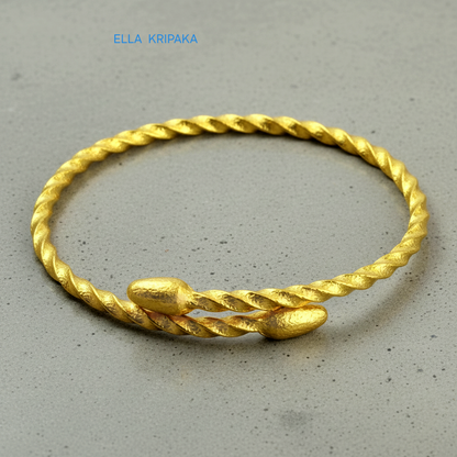 Twisted 24k gold hammered bracelet with oval ends and with textured design on grey polishing concrete surface, branded artist-jeweler 'Ella Kripaka'