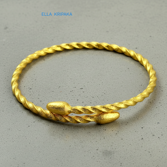 Twisted 24k gold hammered bracelet with oval ends and with textured design on grey polishing concrete surface, branded artist-jeweler 'Ella Kripaka'