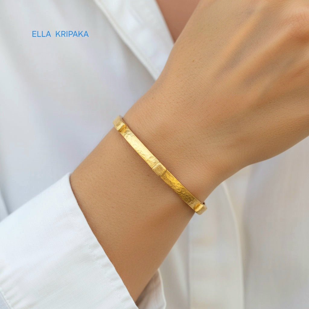 24k gold hammered cuff textured bracelet with thick squares is worn by a woman on wrist and on white shirt background, artist 'Ella Kripaka' branding
