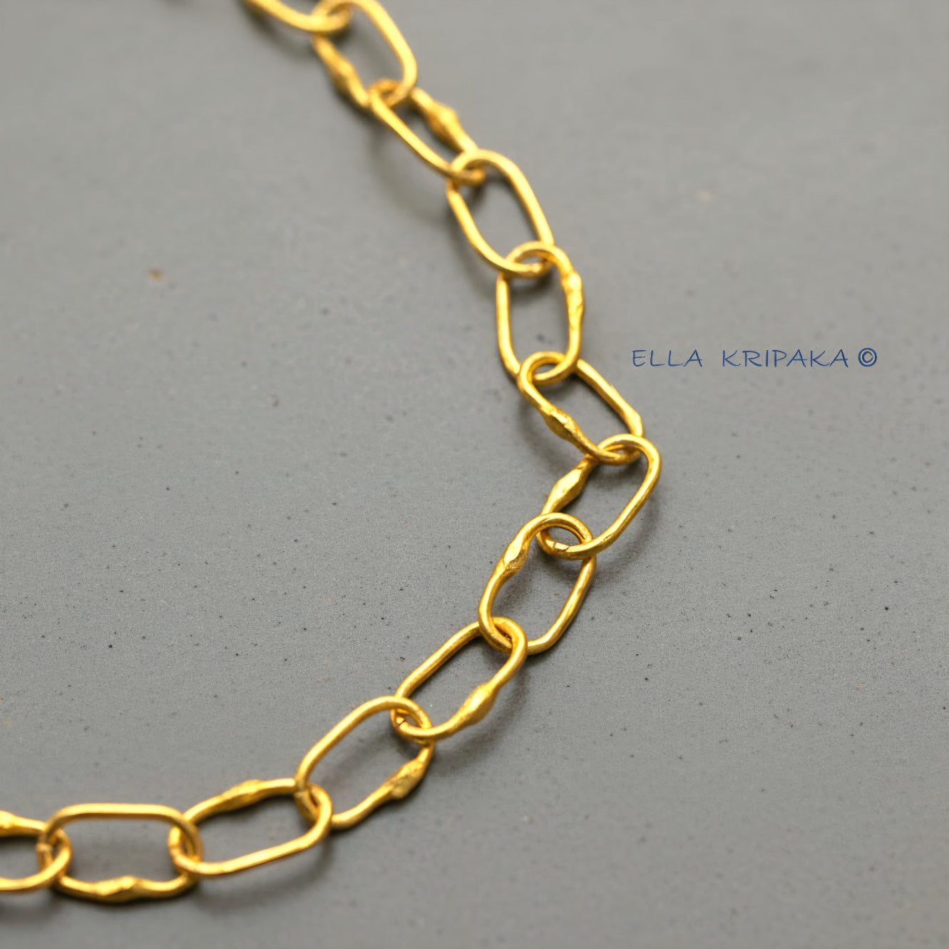 22k gold hammered chain on grey concrete background, artist-jeweler's name 'Ella Kripaka' branding