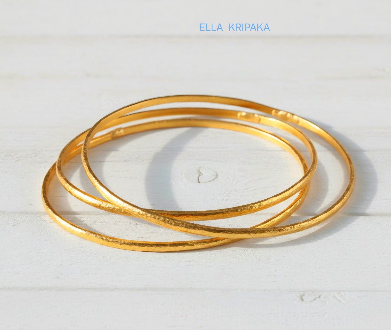 Hammered 22k gold three textured bangles bracelets Ancient Rome style on white wooden surface with 'Ella Kripaka' branding