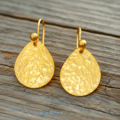 Hammered 24k gold, pure 9999 gold drop earrings with shiny forged gold textures on old wooden surface, artist-jeweler 'Ella Kripaka' branding