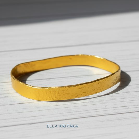 Organic 24k 9999 gold hammered uneven bangle thick bracelet on white wooden surface, artist-jeweler 'Ella Kripaka'