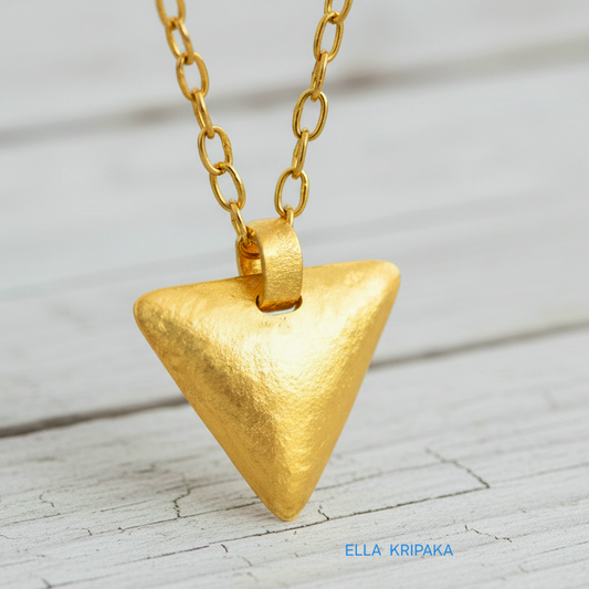 Hammered 24k gold convex triangle pendant with chain on a white rustic wooden background with 'Ella Kripaka' branding