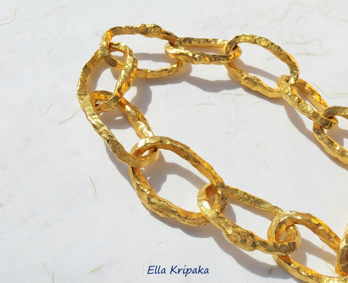 Organic 24k Gold hammered uneven textured chain and uneven edges on a white craft paper surface, with artist 'Ella Kripaka' branding
