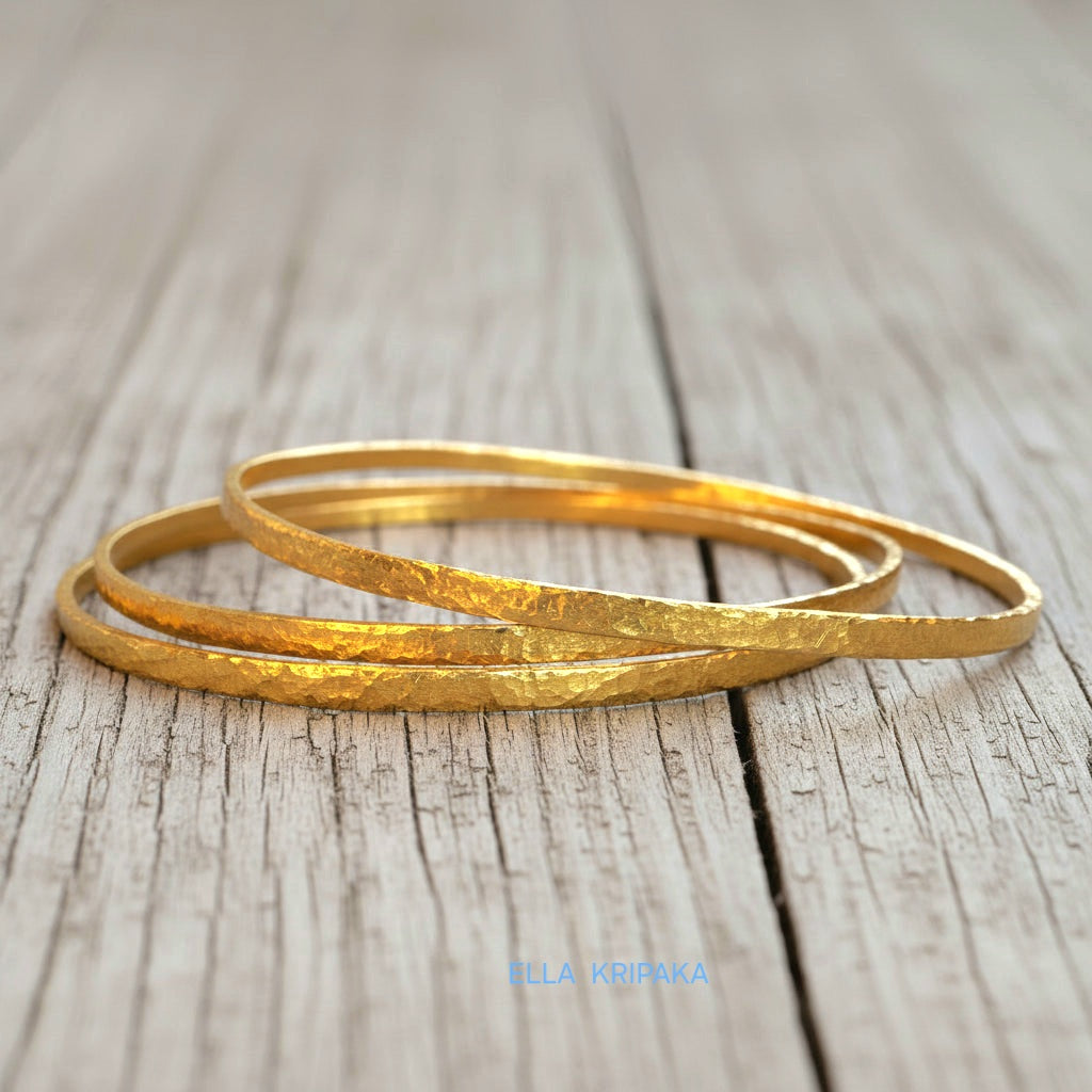 Hammered 22k gold three textured bangles bracelets Ancient Rome style on old wooden surface with 'Ella Kripaka' branding