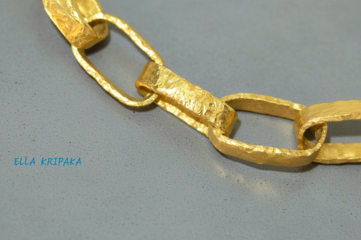 Hammered 24k 9999 gold chain thick necklace Ancient Rome style on a grey concrete background, artist-jeweler name 'Ella Kripaka' branding