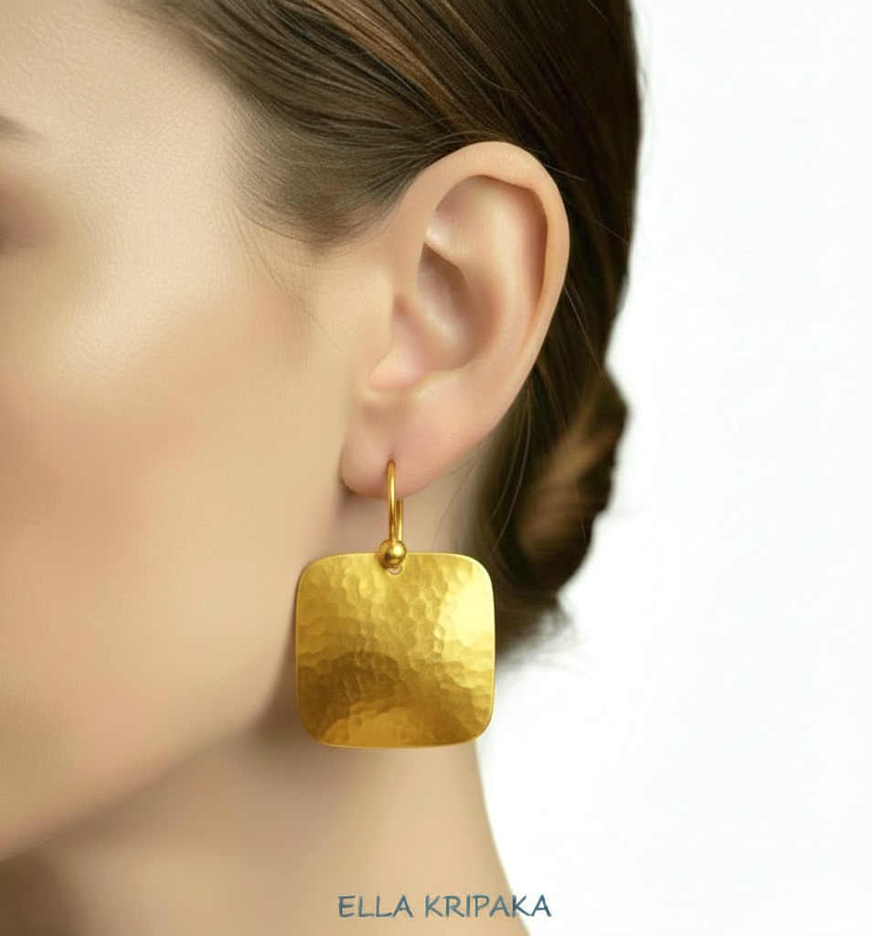 Solid 24k 9999 gold hammered Byzantine earrings with hook clasps and shiny forged gold textures on white old wooden background , artist's name 'ELLA KRIPAKA'