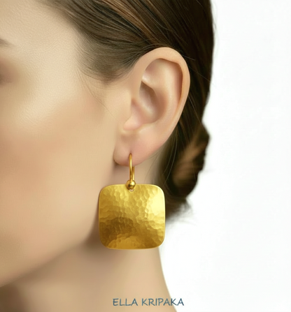 Solid 24k 9999 gold hammered Byzantine earrings with hook clasps and shiny forged gold textures on white old wooden background , artist's name 'ELLA KRIPAKA'