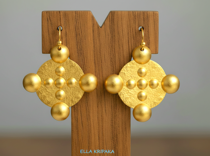 Hammered 24k gold, pure 9999 gold convex rounds Byzantine earring with shiny forged gold textures on a wooden stand and with light grey background, artist-jeweler 'Ella Kripaka' branding