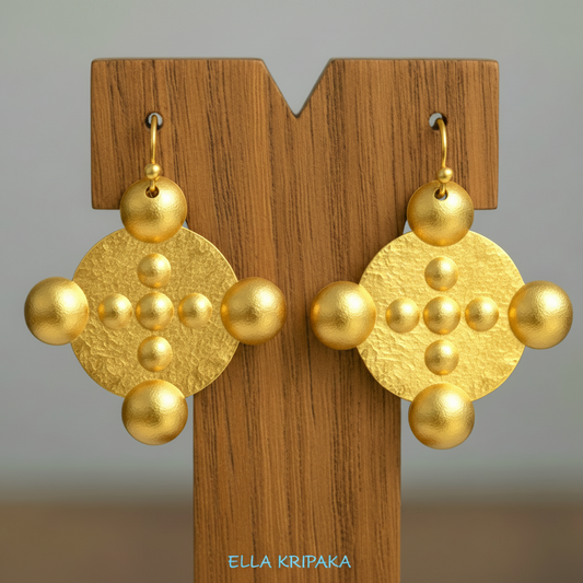 Hammered 24k gold, pure 9999 gold convex rounds Byzantine earring with shiny forged gold textures on a wooden stand and with light grey background, artist-jeweler 'Ella Kripaka' branding