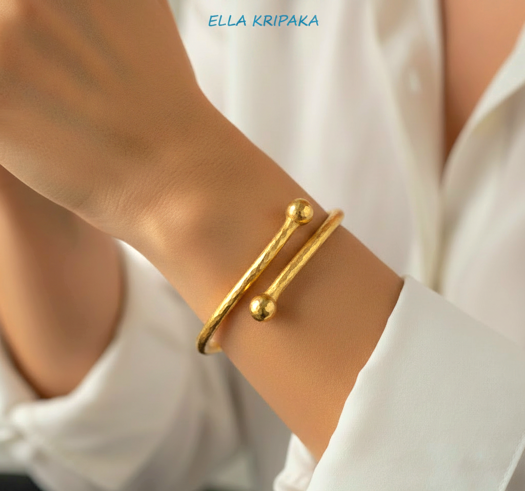 Twisted 24k gold hammered bracelet bangle with convex round ends is worn by a woman on wrist and on white shirt background, branded artist 'Ella Kripaka'
