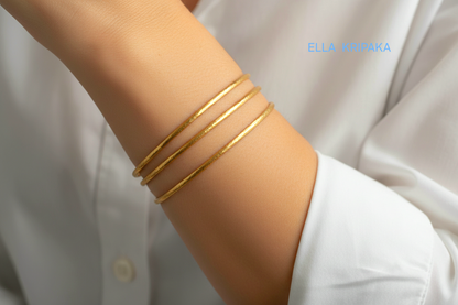Hammered 22k gold three textured bangles bracelets Ancient Rome style on model's wrist and on white blurred shirt background, and with 'Ella Kripaka' branding