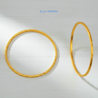 22k gold hammered two thick bangles bracelets Ancient Rome style on a white wooden surface, artist-jeweler 'Ella Kripaka' branding