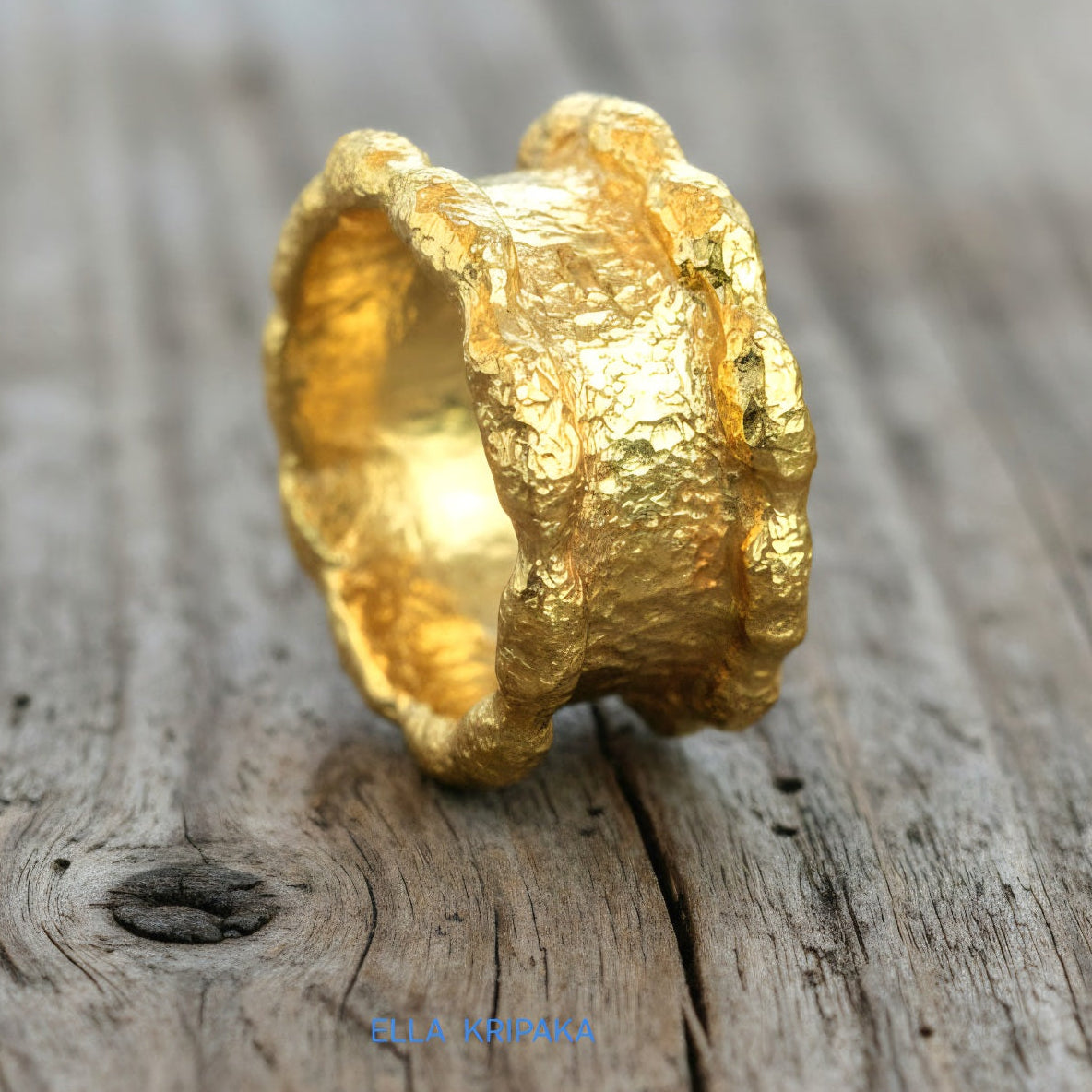Hammered 24k 9999 Gold thick uneven wavy ring organic with a textured gold surface on a old wooden background, branded 'Ella Kripaka'