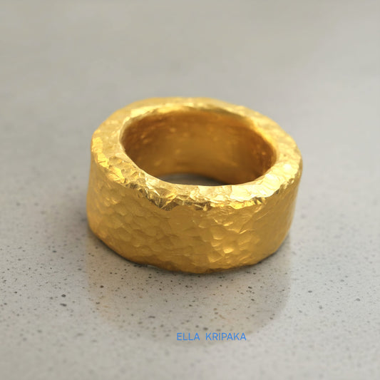 Hammered 24k 9999 Gold thick ring Ancient Rome style with textured gold on a grey concrete background, branded 'Ella Kripaka'