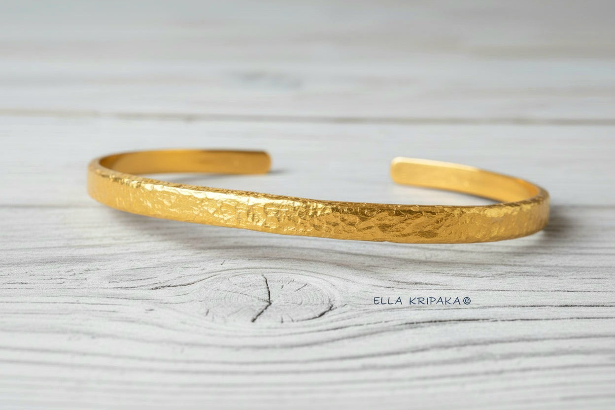 Hammered 24k 9999 gold cuff thick bracelet Ancient Rome style on an old white wooden background, artist-jeweler name 'Ella Kripaka' branding
