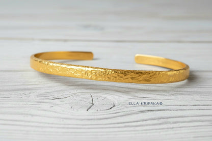 Hammered 24k 9999 gold cuff thick bracelet Ancient Rome style on an old white wooden background, artist-jeweler name 'Ella Kripaka' branding