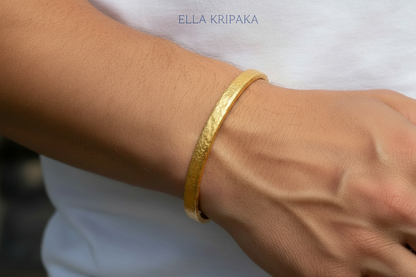 Hammered 24k 9999 gold cuff thick bracelet Ancient Rome style worn by a man on hand and on a white t-shirt background, artist-jeweler name 'Ella Kripaka' branding