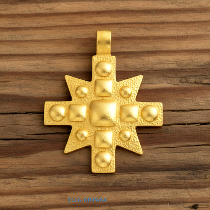 24k gold Byzantine cross pendant textured hammered with convex pattern on brown rustic wooden background, with 'Ella Kripaka' branding