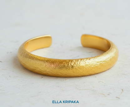 24k 9999 gold hammered cuff bracelet Ancient Rome style on a white craft paper  surface, artist-jeweler 'Ella Kripaka' branding