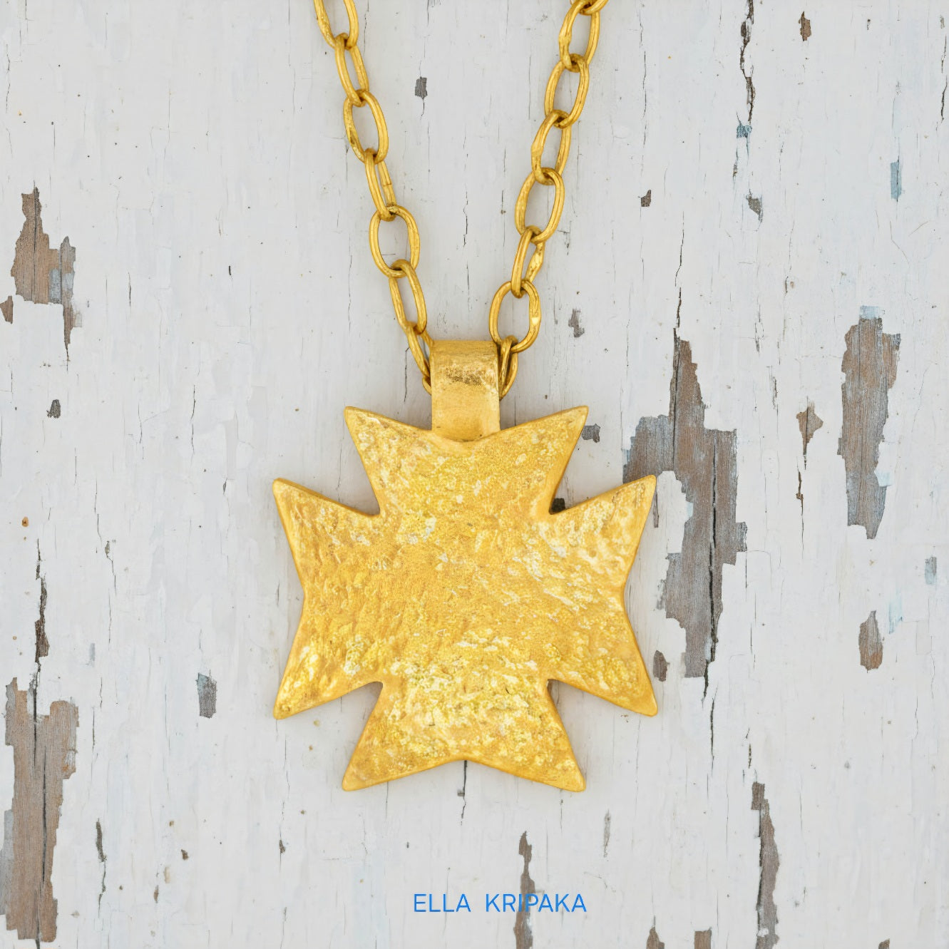 24k gold Byzantine cross pendant textured hammered with chain on old white wooden background, with 'Ella Kripaka' branding