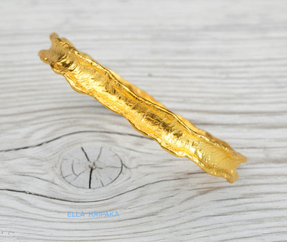 Hammered 22k gold organic textured bangle bracelet with uneven edges on old white wooden surface with 'Ella Kripaka' branding