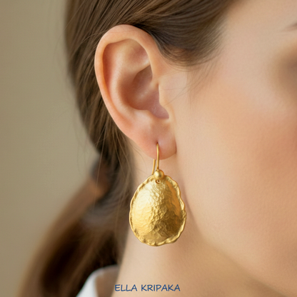 Organic hammered 24k gold, pure 9999 gold convex oval earring with uneven thick edges worn on a woman and with light grey background, artist-jeweler 'Ella Kripaka' branding