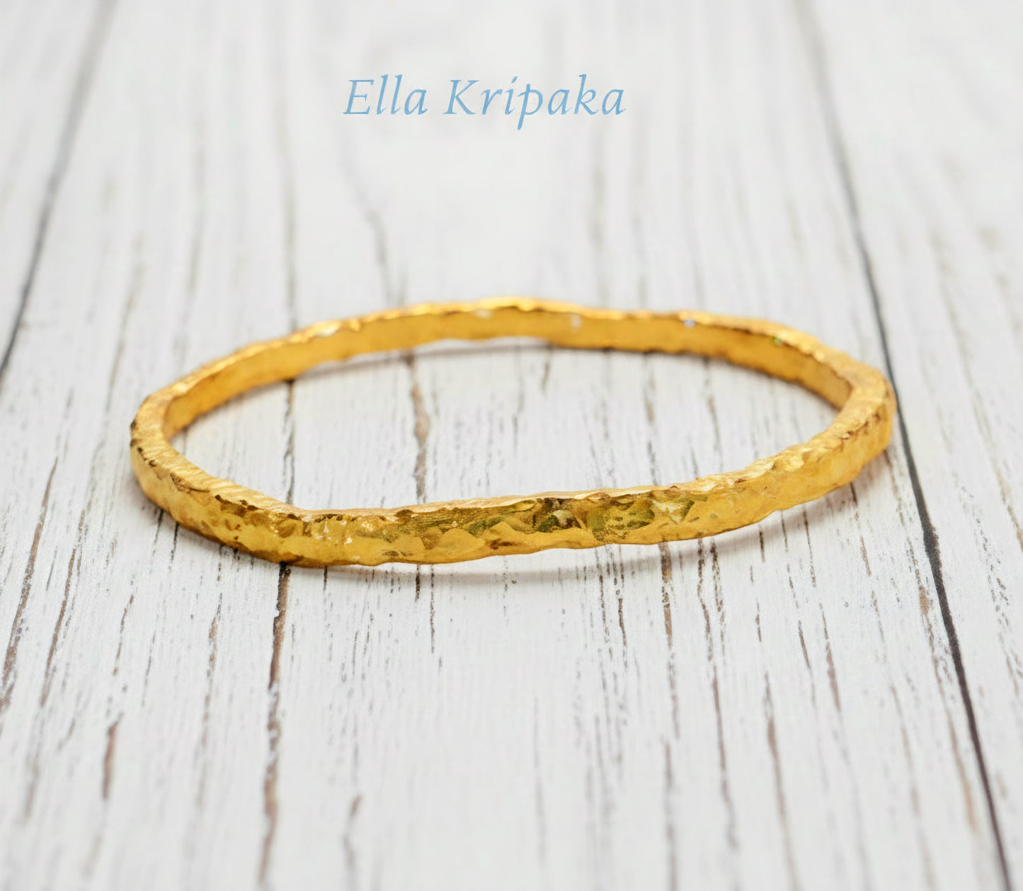 Organic 24k gold textured bangle thick bracelet with uneven edges and on a white wooden background, artist-jeweler name 'Ella Kripaka'