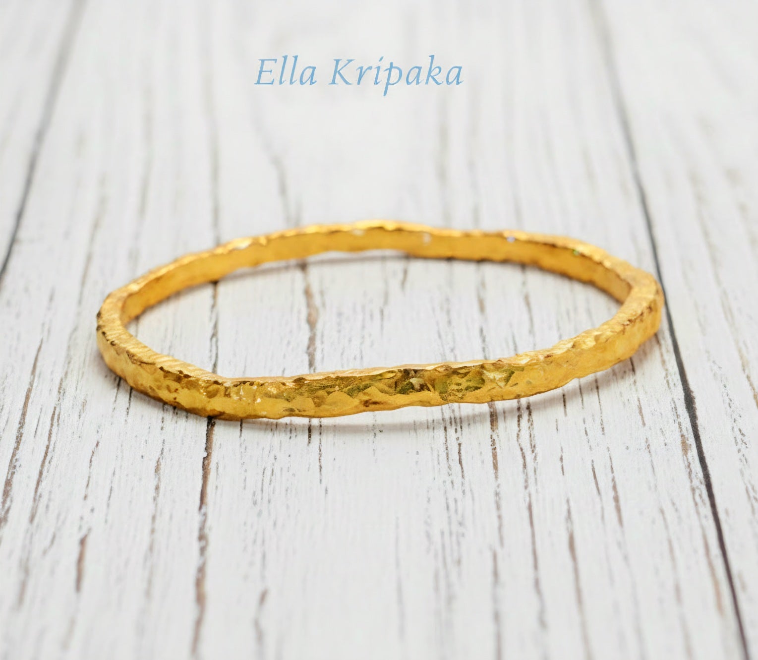 Organic 24k gold textured bangle thick bracelet with uneven edges and on a white wooden background, artist-jeweler name 'Ella Kripaka'