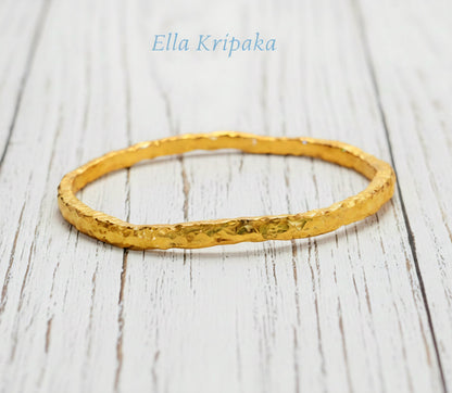 Organic 24k gold textured bangle thick bracelet with uneven edges and on a white wooden background, artist-jeweler name 'Ella Kripaka'