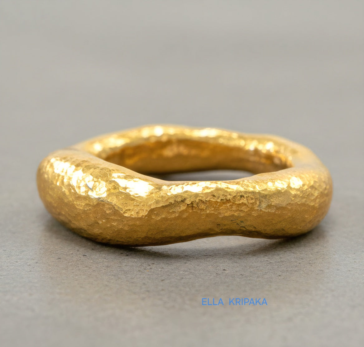Hammered 24k 9999 Gold thick uneven ring organic signet with a textured gold surface on a grey concrete background, branded 'Ella Kripaka'