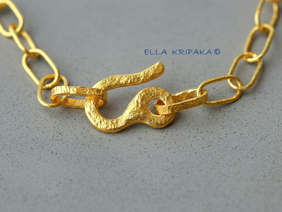 22k gold hammered chain with thick hook clasp on grey concrete background, artist-jeweler's name 'Ella Kripaka' branding
