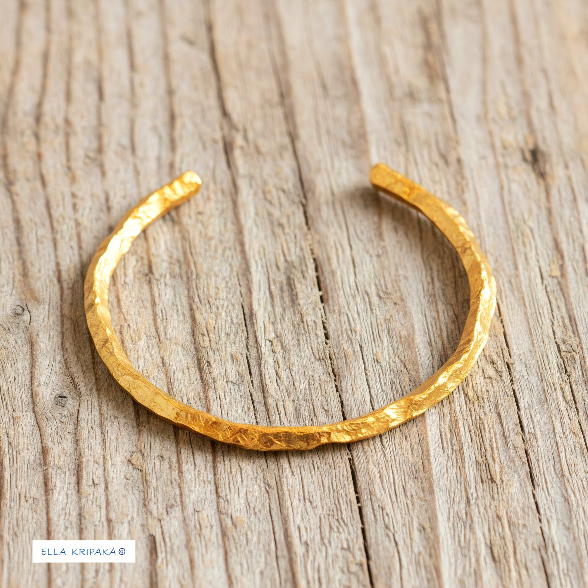 Organic hammered 24k 9999 gold bracelet uneven cuff on a old wooden background, branding artist-jeweler name 'Ella Kripaka'